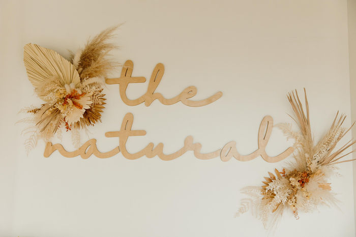 The Natural's hand-script wood sign, flanked by dried florals